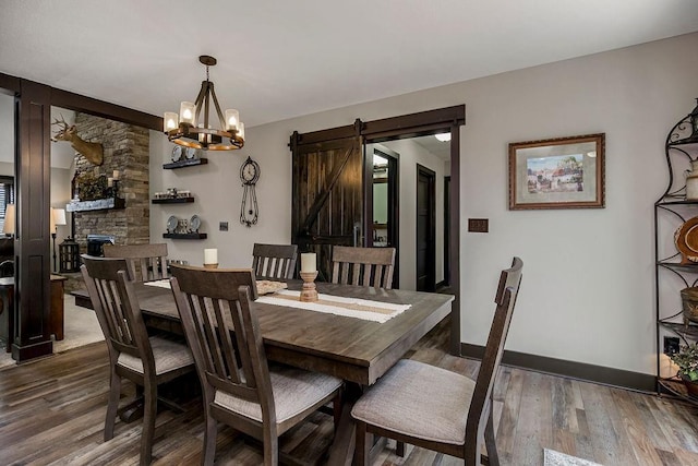 dining area with dark wood-type flooring, a barn door, an inviting chandelier, and a stone fireplace