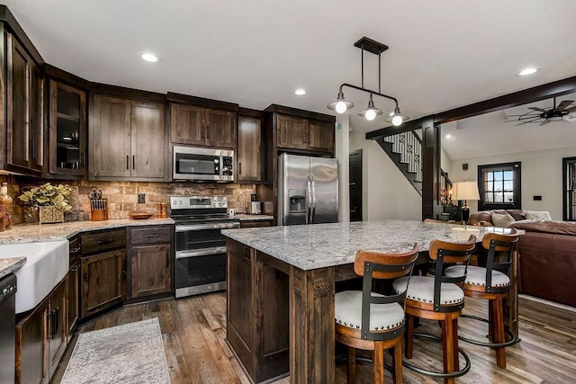 kitchen with dark brown cabinetry, hanging light fixtures, light stone countertops, and appliances with stainless steel finishes