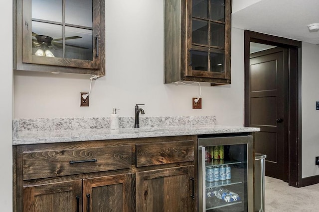 bar with wine cooler, light carpet, light stone countertops, and dark brown cabinetry