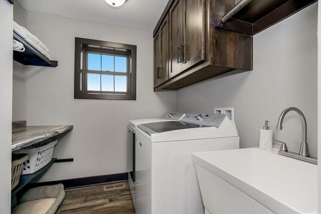 clothes washing area with dark wood-type flooring, cabinets, sink, and washer and dryer