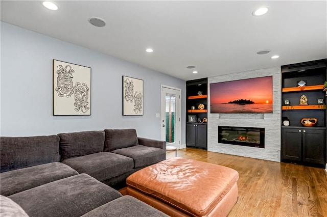 living room with built in shelves, a large fireplace, and hardwood / wood-style floors