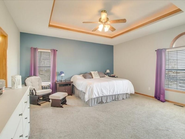 bedroom with light colored carpet, ceiling fan, and a tray ceiling