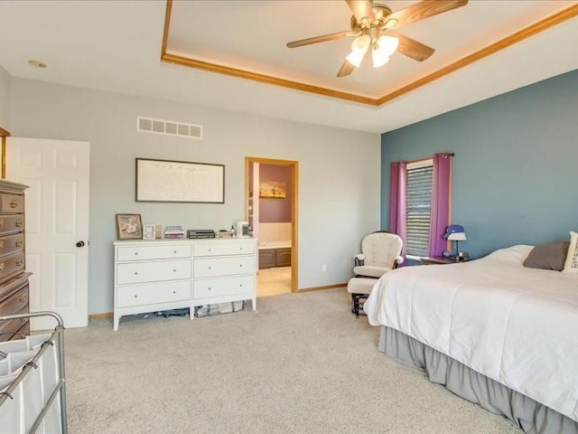 bedroom featuring light carpet, connected bathroom, a tray ceiling, and ceiling fan