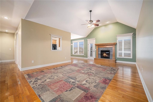 living room with vaulted ceiling, a tiled fireplace, wood finished floors, and baseboards