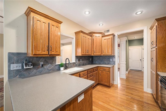 kitchen with sink, ornate columns, light hardwood / wood-style flooring, range with electric cooktop, and decorative backsplash