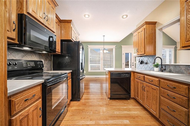 kitchen featuring pendant lighting, sink, black appliances, kitchen peninsula, and light wood-type flooring