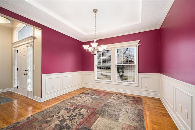 unfurnished dining area with a chandelier, a raised ceiling, wainscoting, and wood finished floors