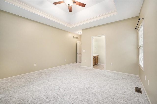 unfurnished bedroom featuring ornamental molding, a tray ceiling, ensuite bath, and light colored carpet