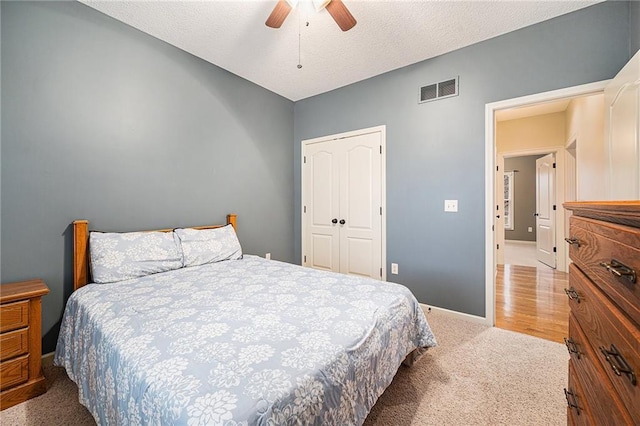 bedroom with ceiling fan, light colored carpet, a closet, and a textured ceiling