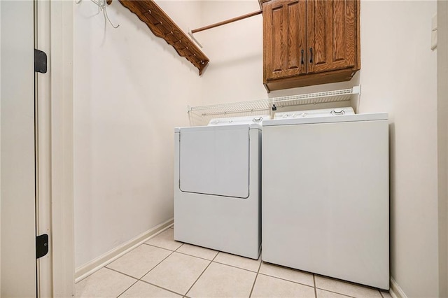 clothes washing area featuring cabinets, light tile patterned flooring, and washing machine and dryer