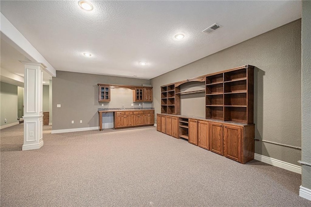 unfurnished living room featuring sink, light colored carpet, decorative columns, and a textured ceiling