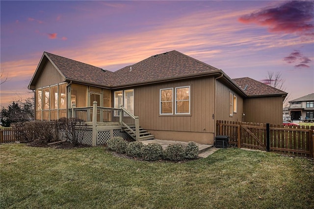 rear view of house featuring a fenced backyard, roof with shingles, and a yard