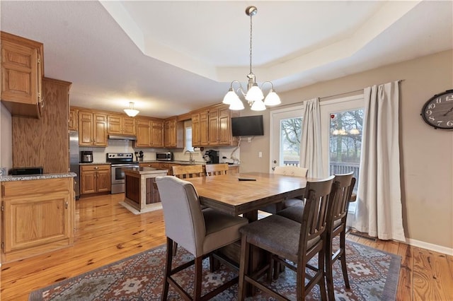 dining area featuring a notable chandelier, a tray ceiling, sink, and light wood-type flooring