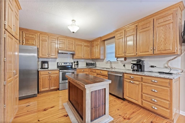 kitchen featuring tasteful backsplash, appliances with stainless steel finishes, light stone countertops, and light hardwood / wood-style floors