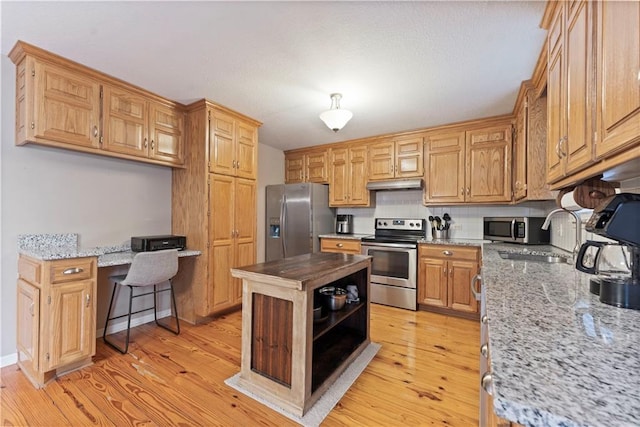 kitchen with sink, light stone counters, built in desk, light hardwood / wood-style flooring, and stainless steel appliances