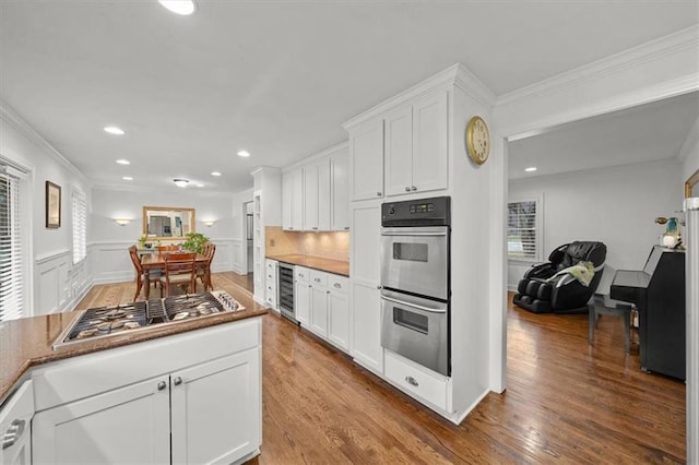 kitchen featuring crown molding, wood-type flooring, stainless steel appliances, beverage cooler, and white cabinets