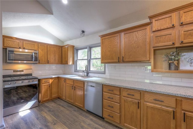 kitchen with sink, appliances with stainless steel finishes, light stone countertops, dark hardwood / wood-style flooring, and vaulted ceiling