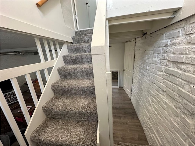 staircase featuring hardwood / wood-style flooring and brick wall