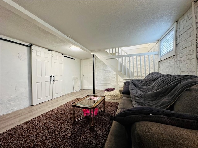 living room with brick wall, a barn door, a textured ceiling, and light wood-type flooring