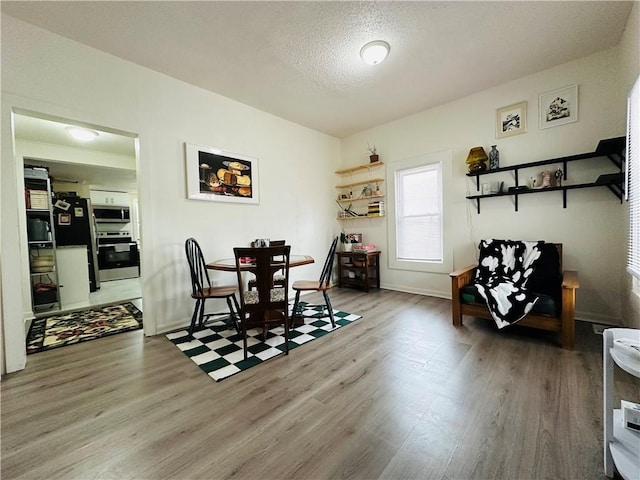 dining area featuring a textured ceiling, baseboards, and wood finished floors