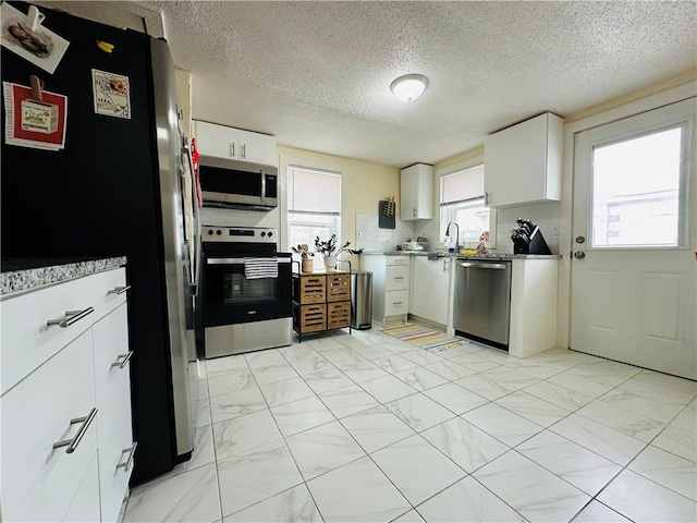 kitchen with white cabinets, a sink, a textured ceiling, marble finish floor, and stainless steel appliances