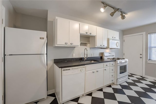 kitchen featuring white appliances, a sink, white cabinets, dark countertops, and tile patterned floors