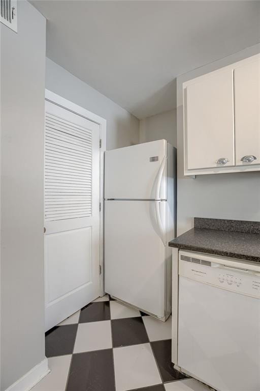 kitchen with tile patterned floors, white appliances, dark countertops, and white cabinetry