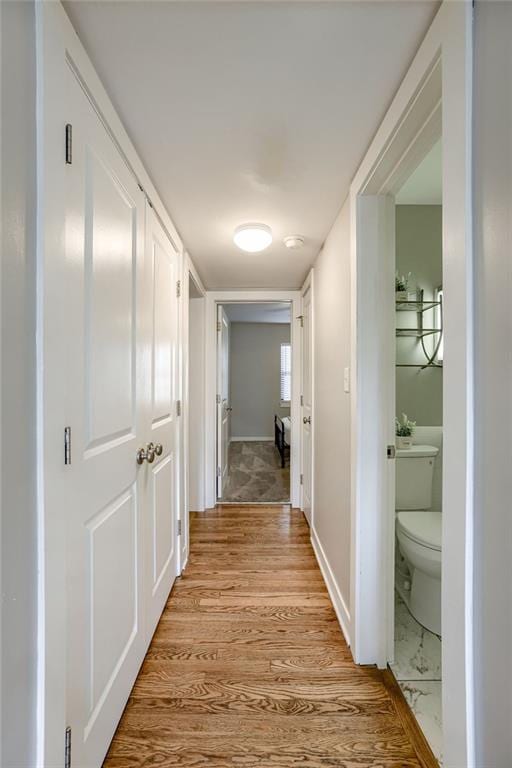 hallway featuring light wood finished floors and baseboards