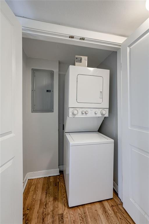 clothes washing area featuring electric panel, laundry area, light wood-type flooring, and stacked washer / drying machine