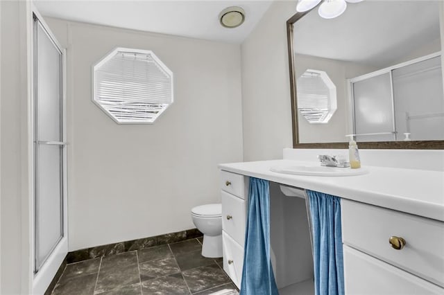 bathroom featuring toilet, vanity, a stall shower, and baseboards