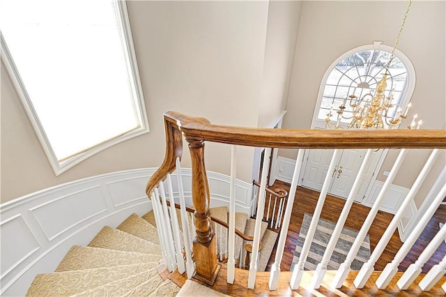 stairway featuring an inviting chandelier, a decorative wall, wood finished floors, and wainscoting