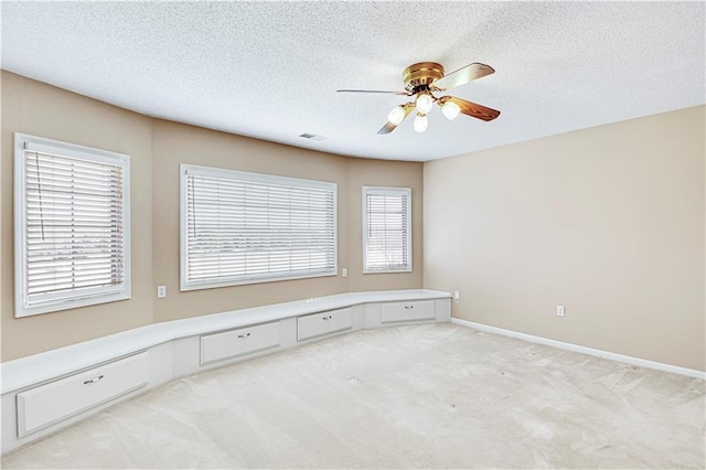 unfurnished room with a ceiling fan, baseboards, built in desk, a textured ceiling, and light colored carpet