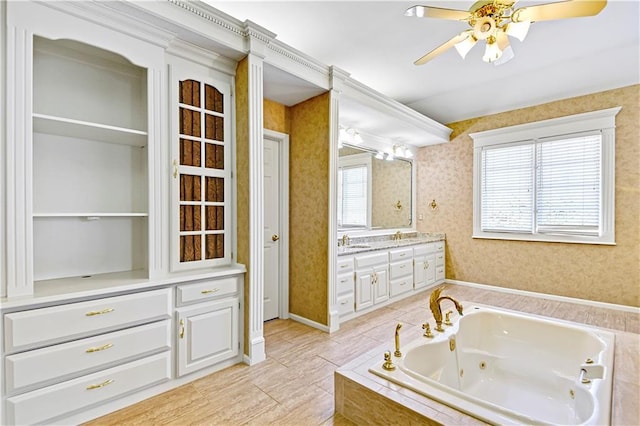 full bath featuring a tub with jets, wallpapered walls, baseboards, ceiling fan, and vanity