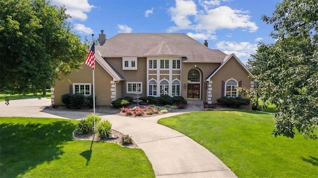 tudor-style house with a front lawn, a chimney, driveway, and stucco siding