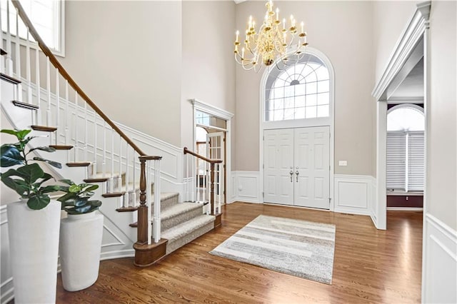 entryway featuring a chandelier, a wainscoted wall, a towering ceiling, and wood finished floors