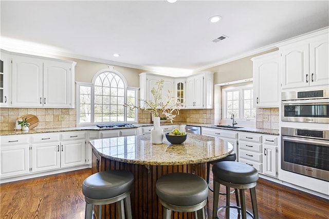 kitchen with visible vents, ornamental molding, glass insert cabinets, a kitchen breakfast bar, and a center island