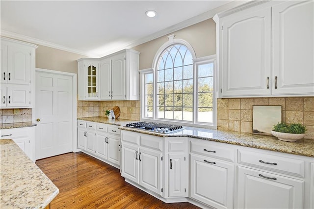 kitchen with light stone counters, dark wood-style floors, stainless steel gas cooktop, ornamental molding, and white cabinetry