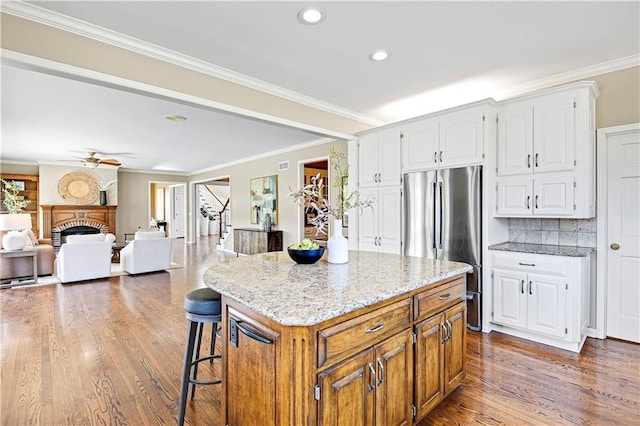 kitchen with dark wood-type flooring, light stone countertops, decorative backsplash, a fireplace, and freestanding refrigerator