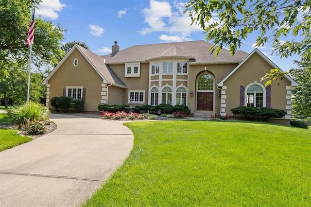 view of front of house with stucco siding, driveway, a chimney, and a front lawn