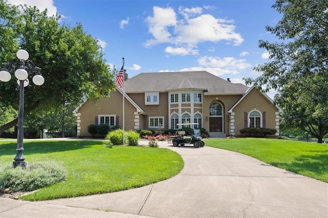 view of front of house with a front yard, concrete driveway, a chimney, and stucco siding