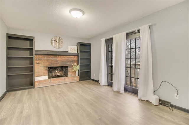 unfurnished living room with built in shelves, a textured ceiling, a brick fireplace, and light hardwood / wood-style flooring