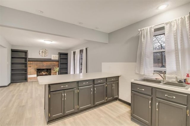 kitchen with sink, gray cabinetry, light hardwood / wood-style flooring, a brick fireplace, and kitchen peninsula