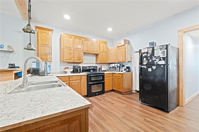 kitchen featuring decorative light fixtures, light countertops, light wood-style floors, a sink, and black appliances