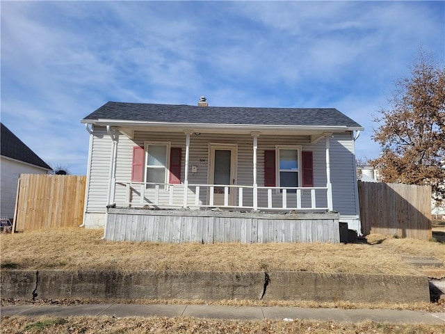 view of front facade with covered porch, a shingled roof, and fence