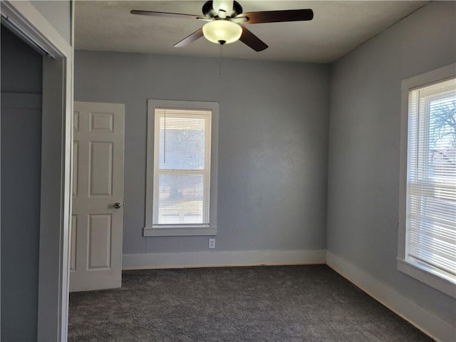 unfurnished room with ceiling fan, dark colored carpet, and baseboards