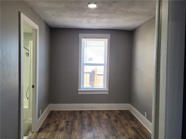 unfurnished room with dark wood-style flooring, a textured ceiling, and baseboards