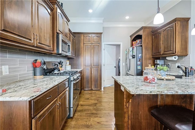 kitchen with sink, crown molding, a breakfast bar, appliances with stainless steel finishes, and hardwood / wood-style floors