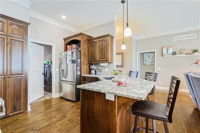 kitchen with stainless steel refrigerator with ice dispenser, a breakfast bar, washing machine and clothes dryer, and light stone counters