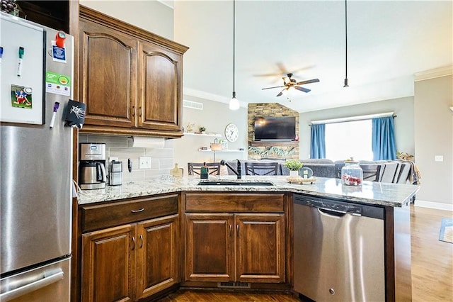 kitchen featuring sink, tasteful backsplash, light stone counters, hanging light fixtures, and appliances with stainless steel finishes