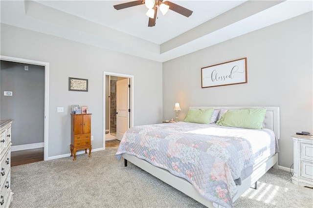 bedroom featuring a raised ceiling, light colored carpet, ceiling fan, and ensuite bath